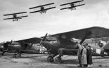 Breguet XIX na lotnisku, nad którym akrobacje wykonują piloci trójki Bajana w myśliwcach PWS-A. Tydzień Ligi Obrony Powietrznej i Przeciwgazowej w Katowicach, maj 1933 r. (Źródło: NAC sygn. 3/1/0/7/2737/3).